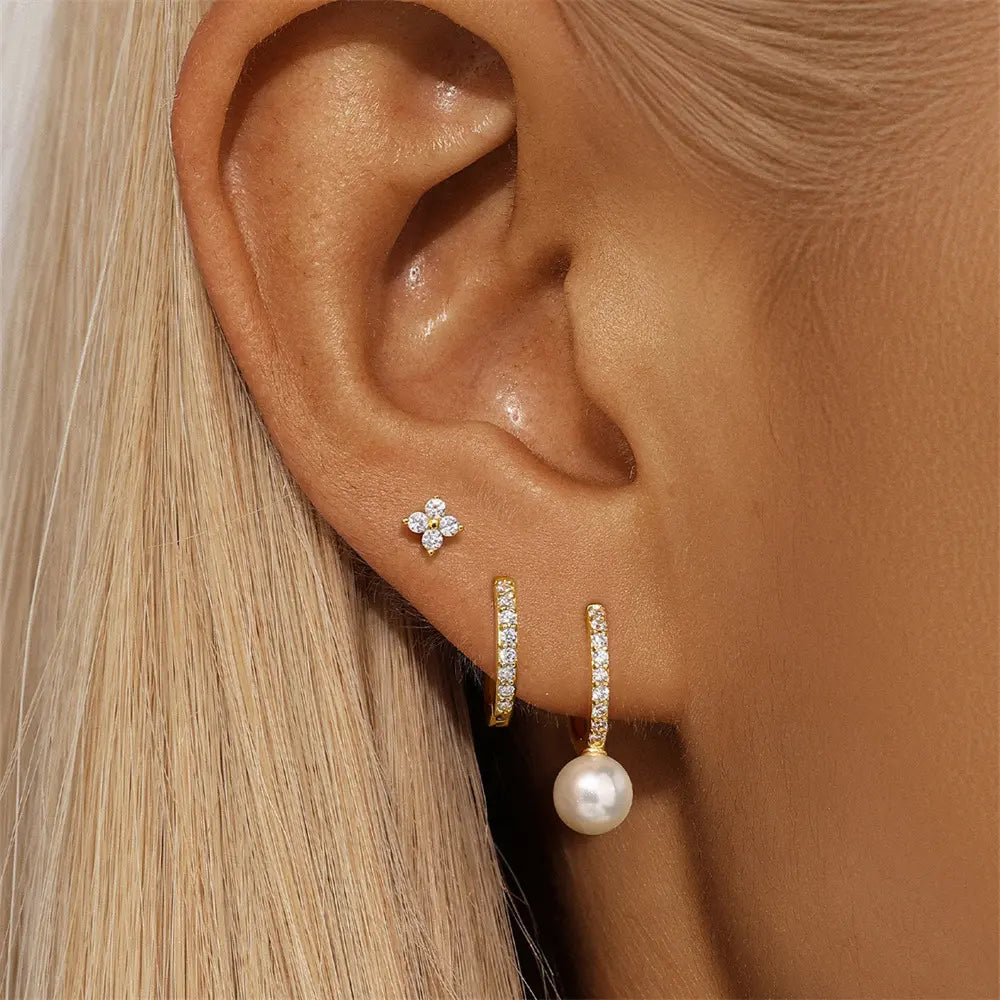 Gold hoop earrings with cubic zirconia and pearl drop, paired with a small cubic zirconia stud on a model's ear.