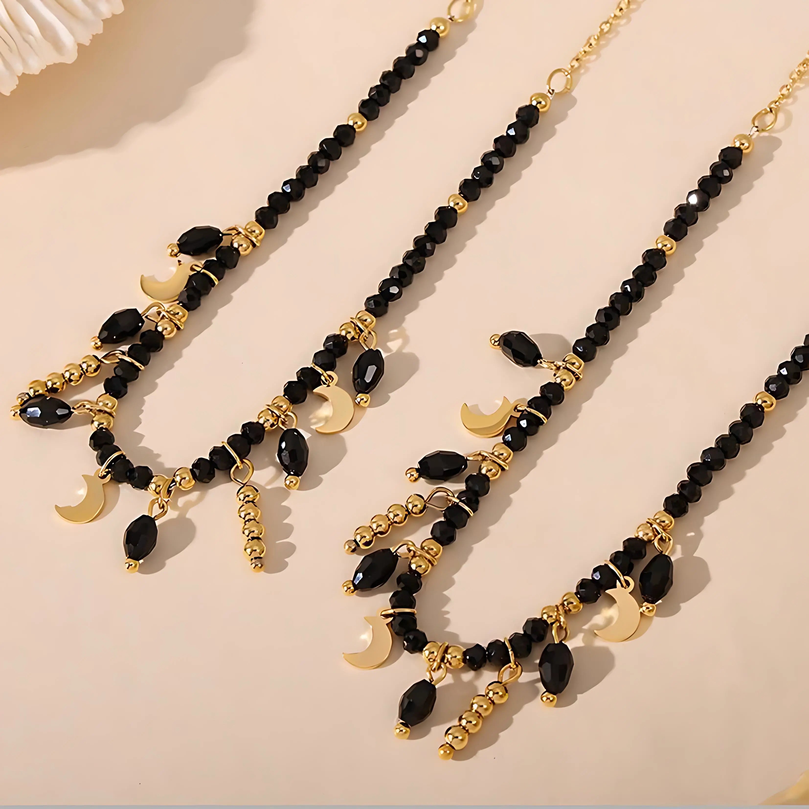 A close-up view of gold and black bead necklaces featuring crescent moon charms, laid stylishly for a modern vibe.