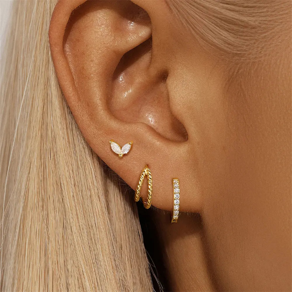 Close-up of a model's ear adorned with gold marquise stud, twisted rope huggie hoop, and a pave stone huggie hoop earring.