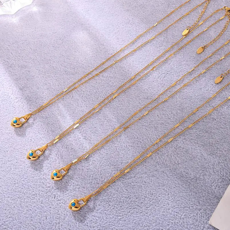 Multiple gold heart-shaped padlock necklaces with turquoise stones laid out on a soft, light purple textured background.