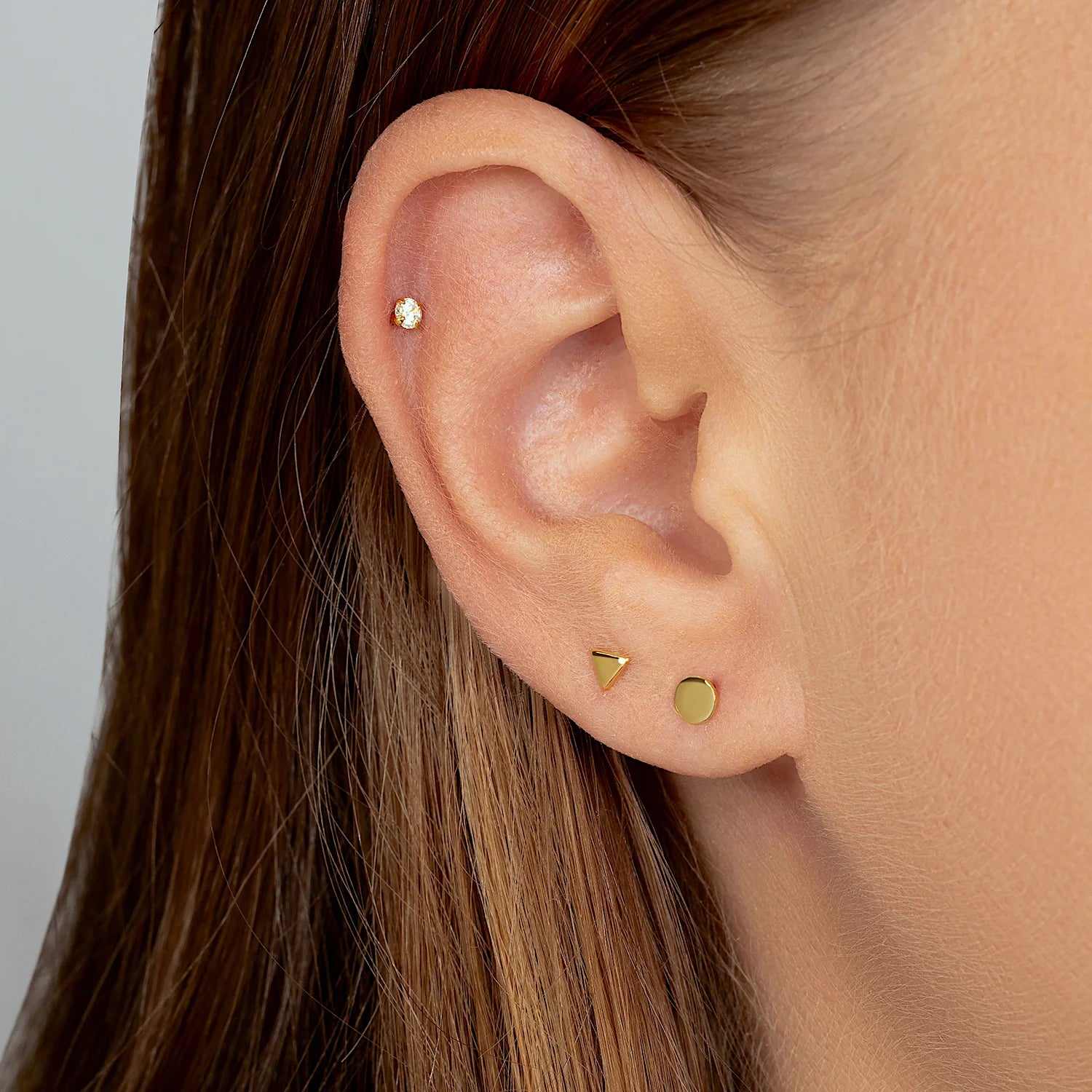 Model wearing a 14K gold flat disc stud earring in a chic minimalist ear stack.
