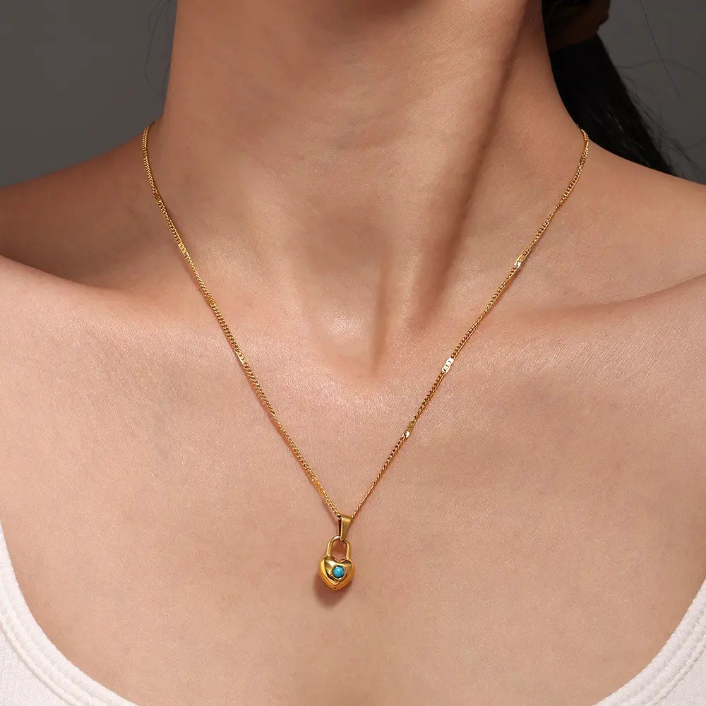 A gold heart-shaped padlock necklace with a turquoise stone worn by a model, showcasing the elegant fit around the neckline.