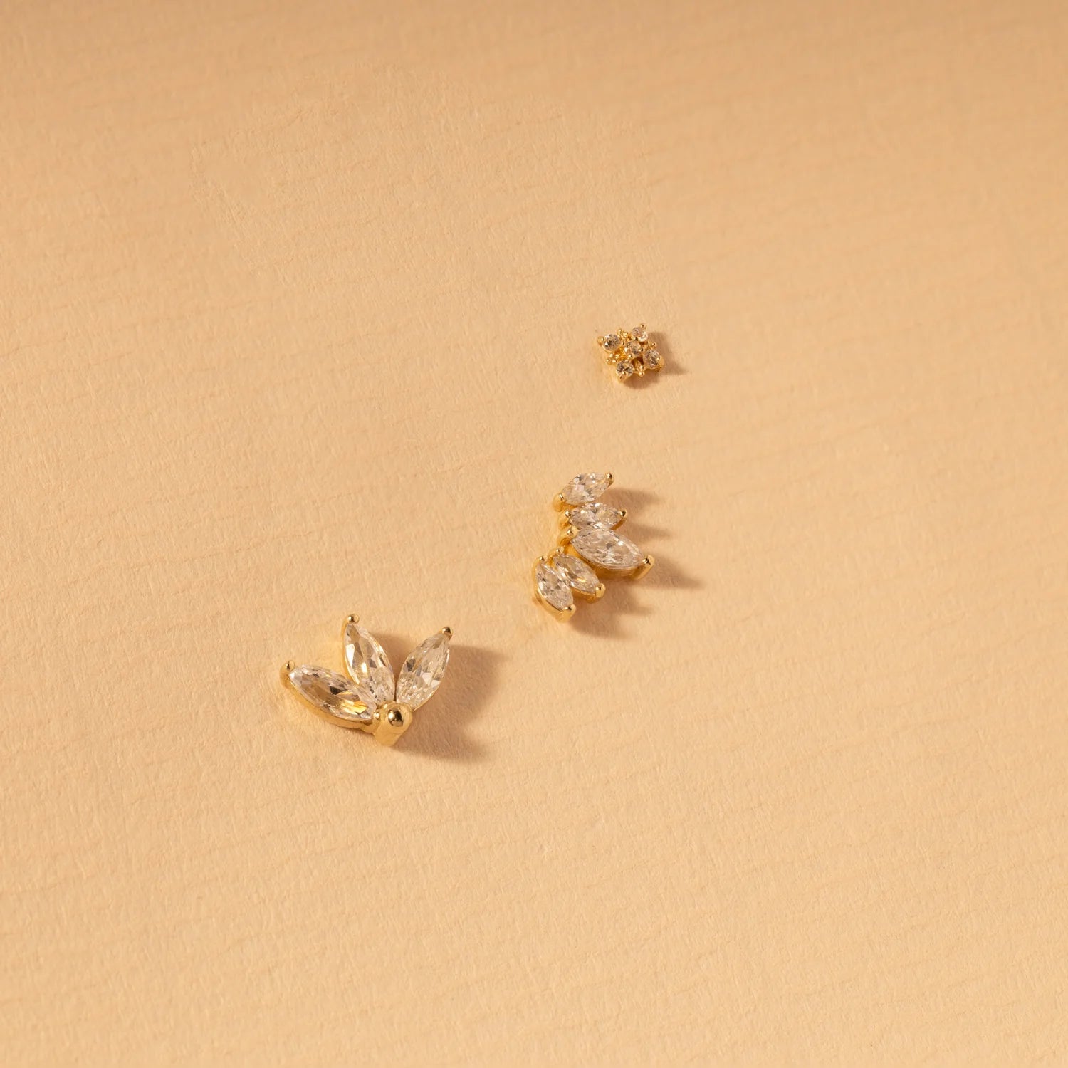 Flatlay of 14K gold triple leaf stud earring with matching jewelry pieces on a soft beige background.