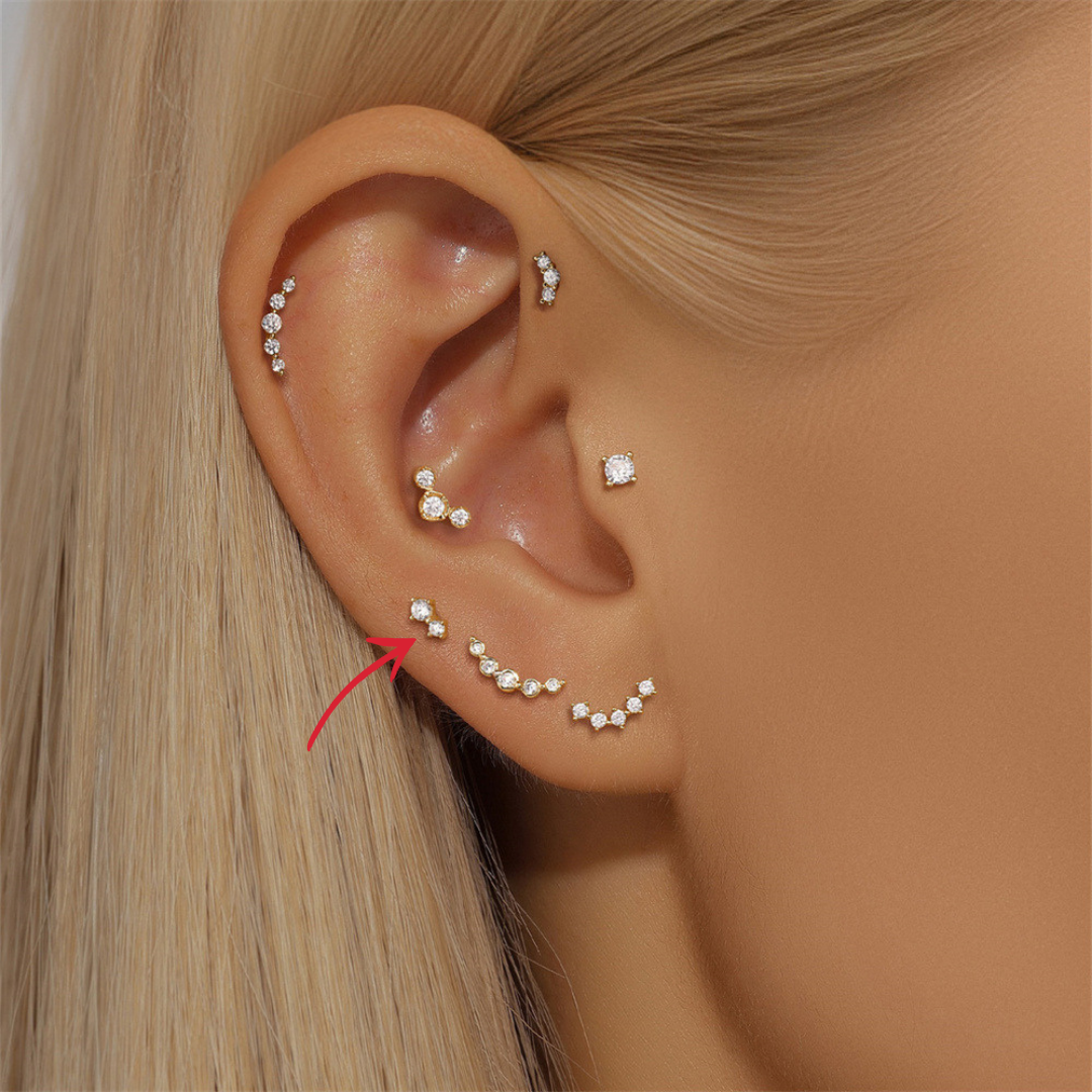 Woman wearing a 14K gold triple zircon stud earring, styled with other dainty gold earrings.