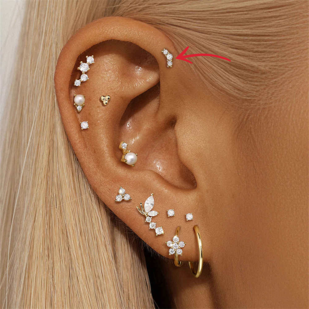 A model wearing a 14K gold curved stud earring with three zirconia stones in an ear-stacking look.