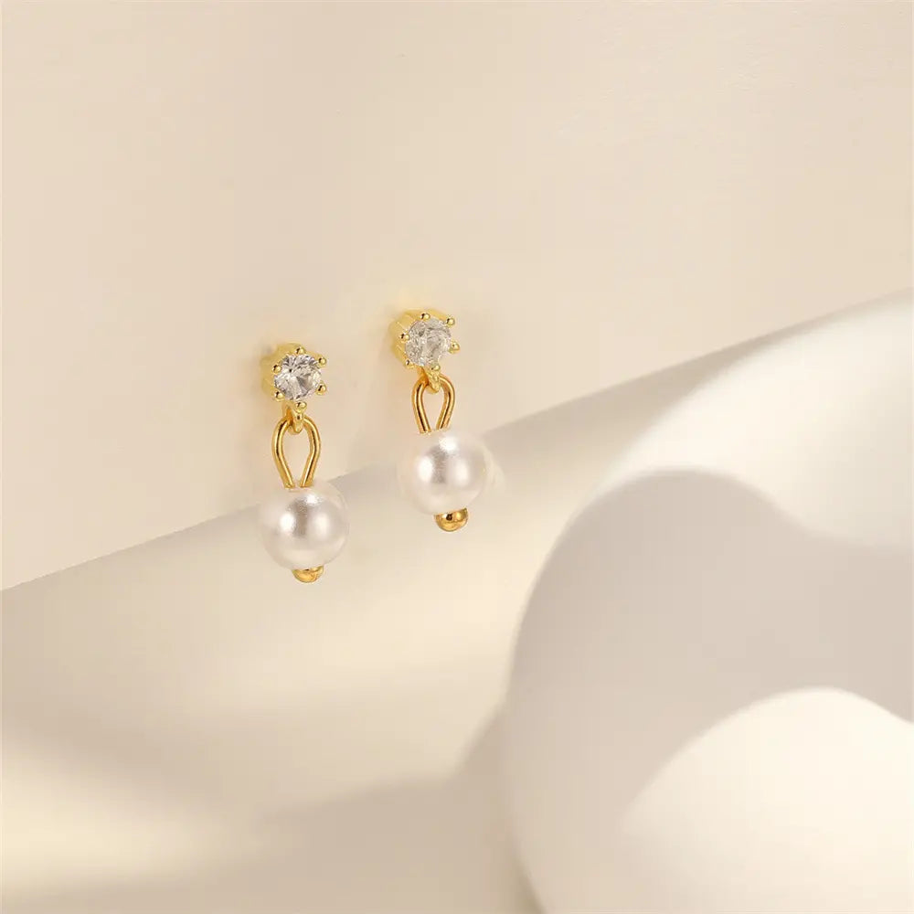 Gold dangle earrings with sparkling crystal studs and elegant pearl drops, displayed on a neutral background for a timeless and sophisticated design.