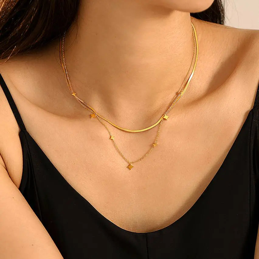 Close-up of a woman's neckline wearing a layered gold necklace featuring a smooth, curved design and a dainty star charm chain.