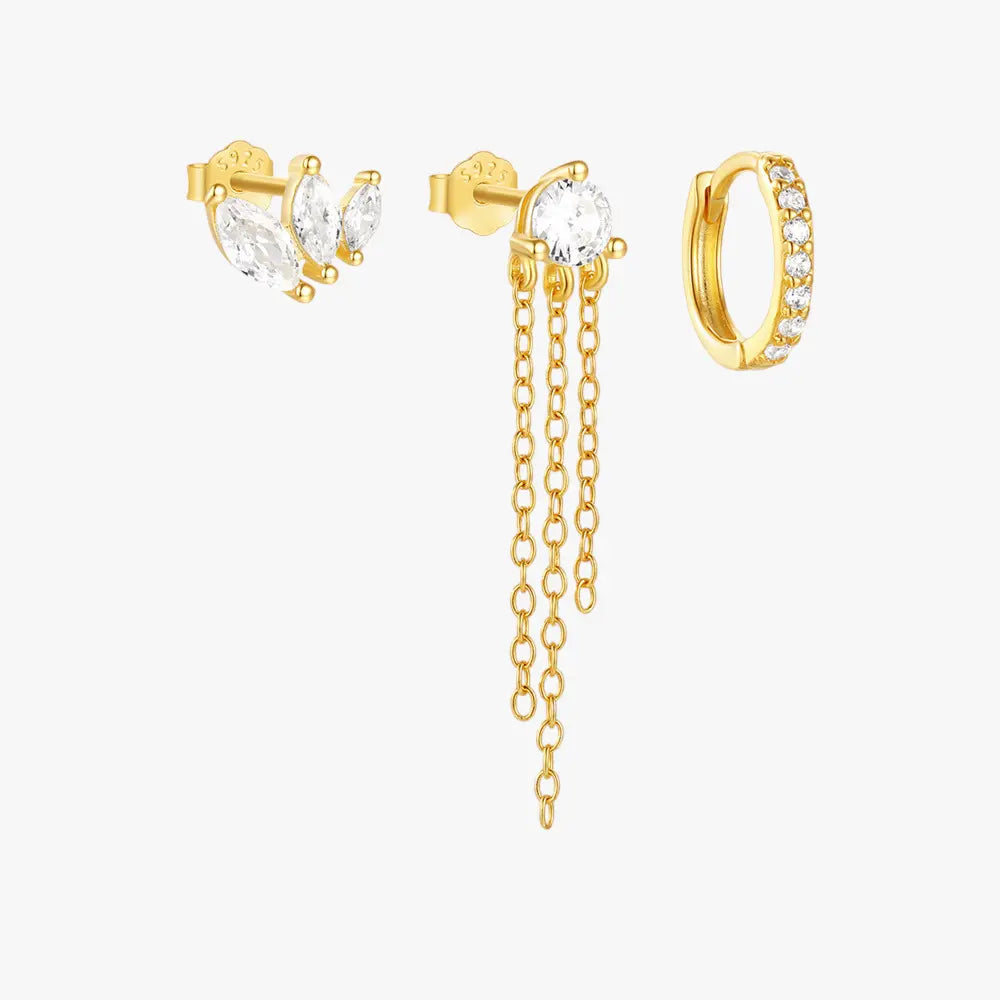 Gold triple earring set featuring marquise-shaped zircon studs, a round zircon stud with gold chain dangles, and a crystal-encrusted hoop earring.