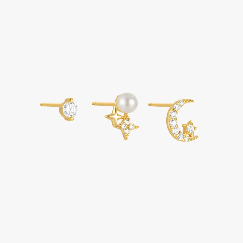 Three mismatched gold stud earrings with celestial motifs: a classic clear round stone, a gold star with a small pearl, and a crescent moon adorned with sparkling crystals.