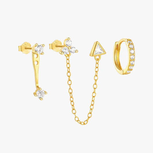 A set of three mismatched gold earrings, including a triangle charm with a chain, a stud with a curved bar, and a small hoop with crystals.