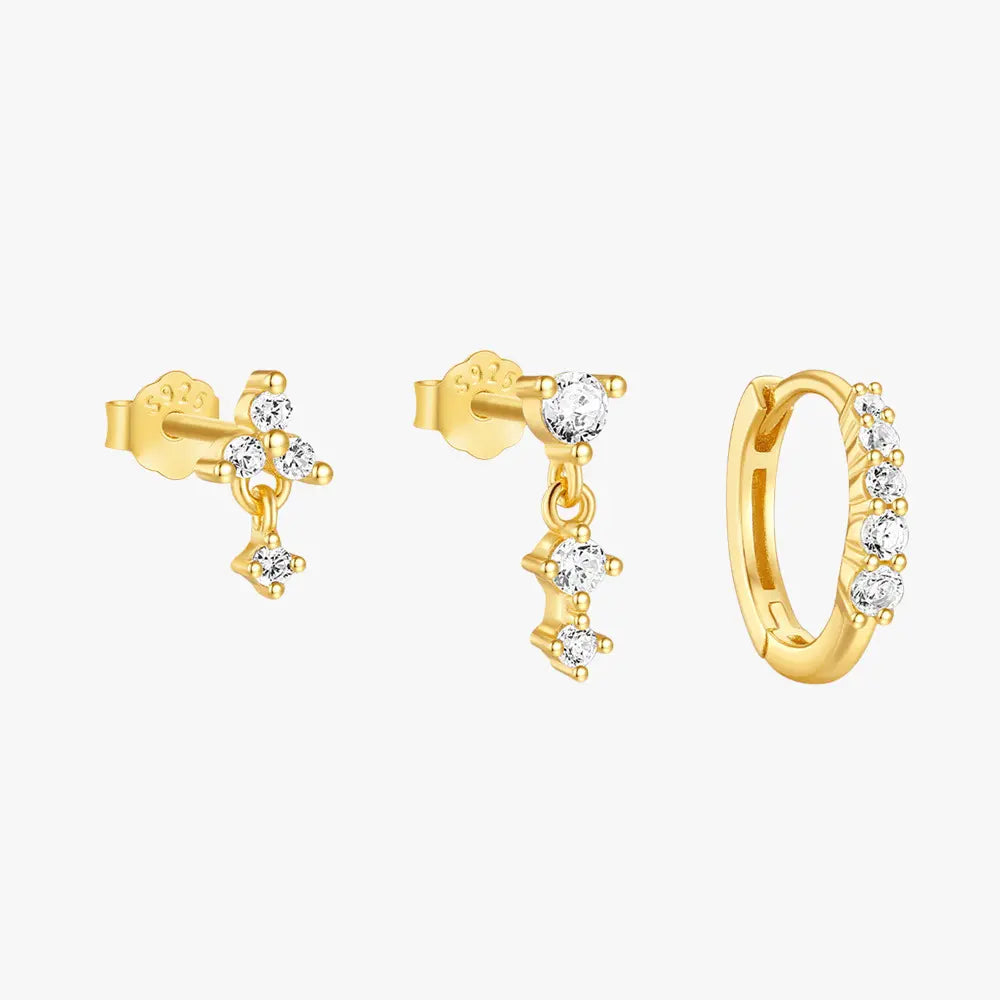 A set of three gold earrings featuring clear gemstones: a small stud, a dangling gem with three connected stones, and a gold hoop earring adorned with sparkling gems.