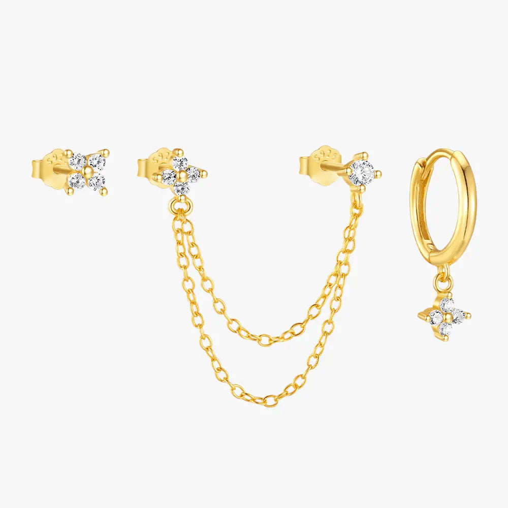 A set of three gold-plated earrings with sparkling zircon stones. Includes a dainty stud, a double-chain dangling earring, and a gold hoop with a flower-shaped zircon pendant.