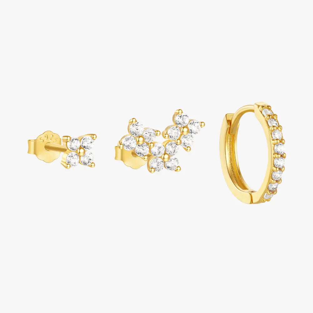 A set of three gold earrings with cubic zirconia stones, including two stud earrings with floral cluster designs and a gold hoop earring with small sparkling stones along its edge.