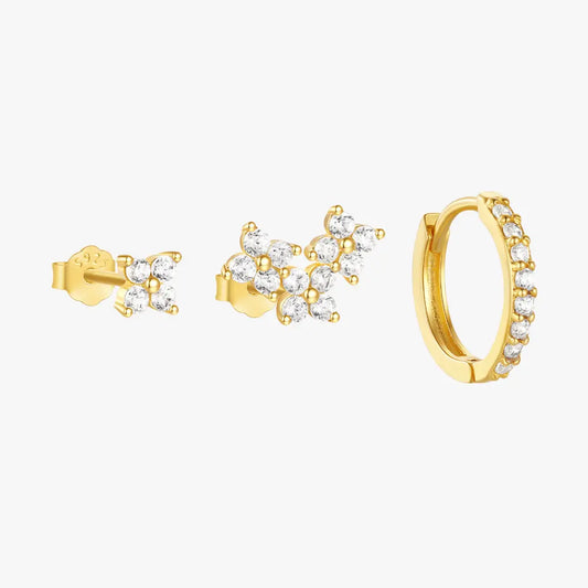 A set of three gold earrings with cubic zirconia stones, including two stud earrings with floral cluster designs and a gold hoop earring with small sparkling stones along its edge.