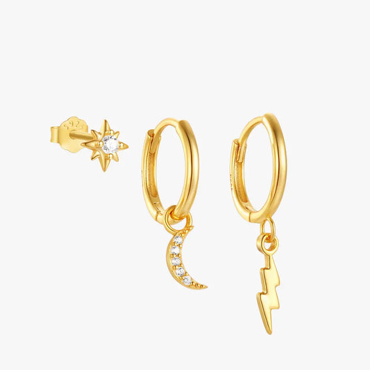 A gold set of three earrings, including a star-shaped stud with a central gemstone, a crescent moon charm hoop earring adorned with small diamonds, and a lightning bolt charm hoop earring.