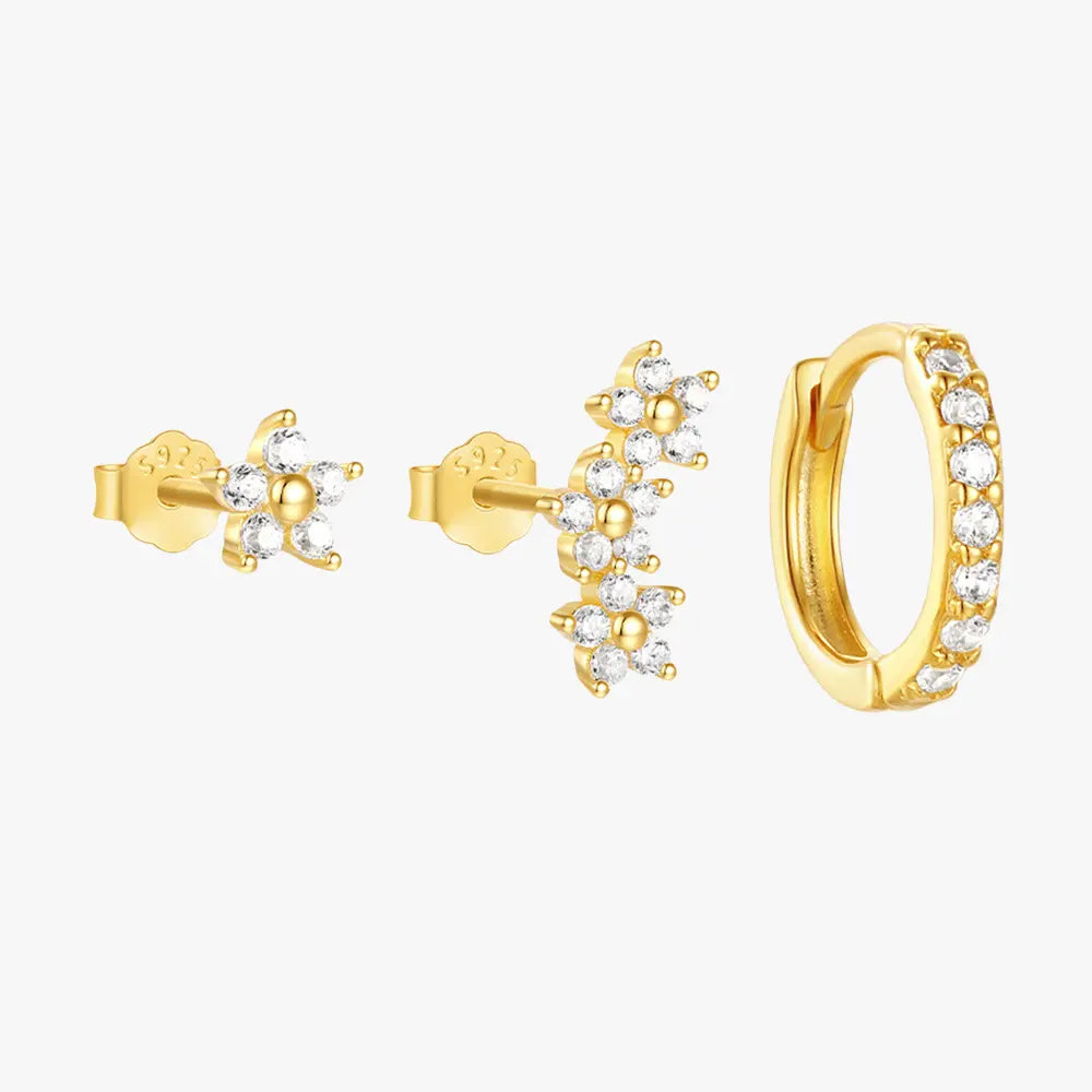 A set of three gold-plated earrings featuring flower-shaped studs with sparkling cubic zirconia stones, and a huggie hoop adorned with pave-set crystals.