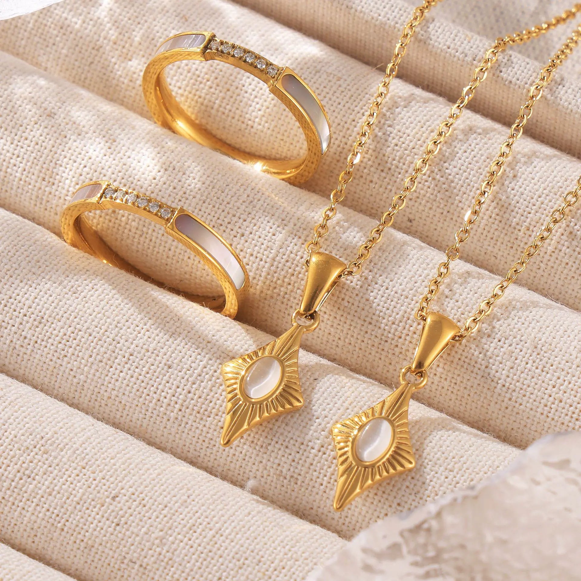 Two gold diamond-shaped necklaces with oval centerstones, displayed alongside matching gold rings with similar designs.