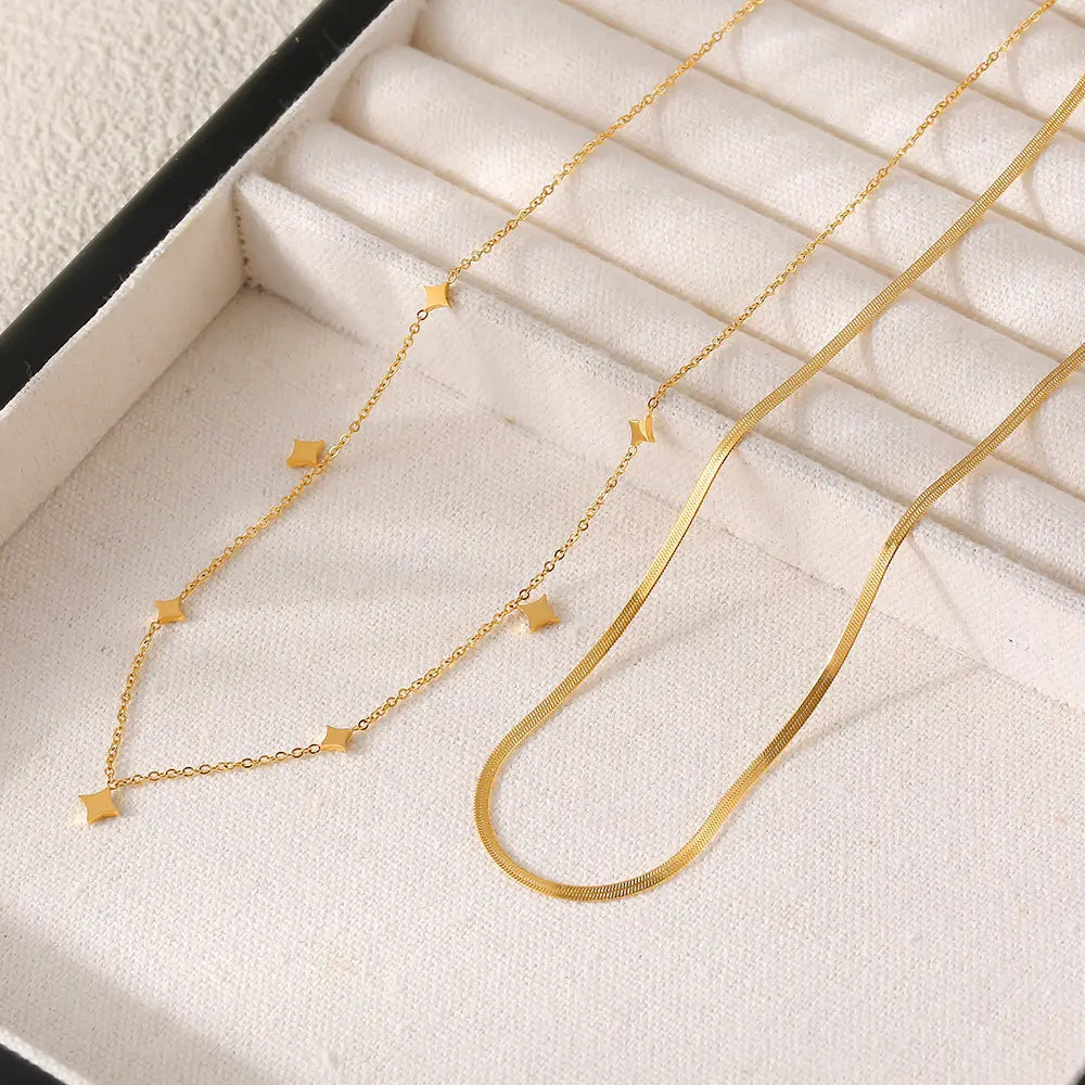 Two gold necklaces displayed in a jewelry box, one with a sleek curved design and another with small star charms.