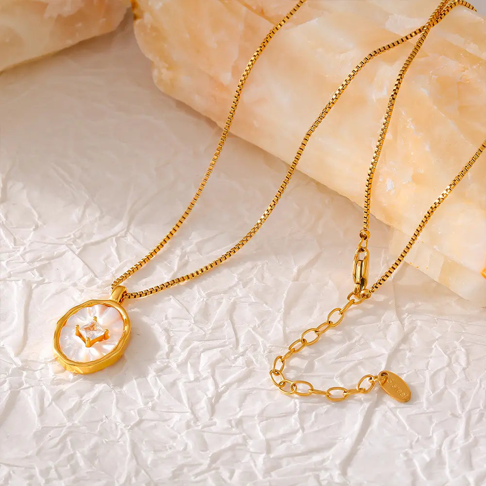 Close-up of a gold-plated oval pendant necklace placed on a crinkled beige surface.