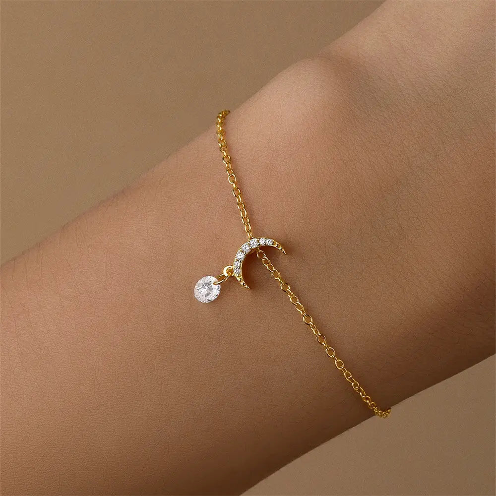 Close-up of a gold crescent moon bracelet with a sparkling crystal charm, worn on a wrist.