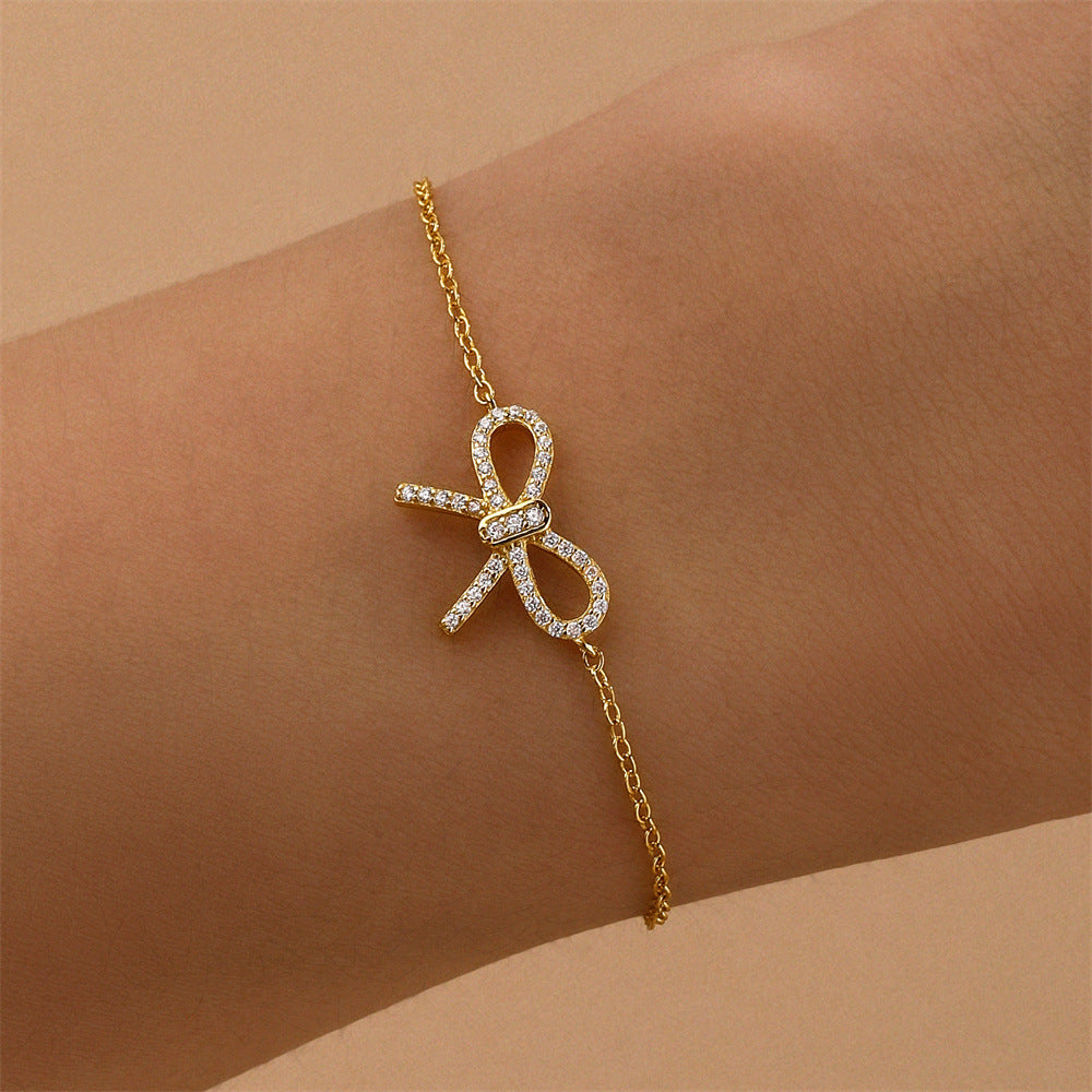 Elegant gold bracelet featuring a sparkling bow pendant worn on the wrist, showcasing a dainty and luxurious design.