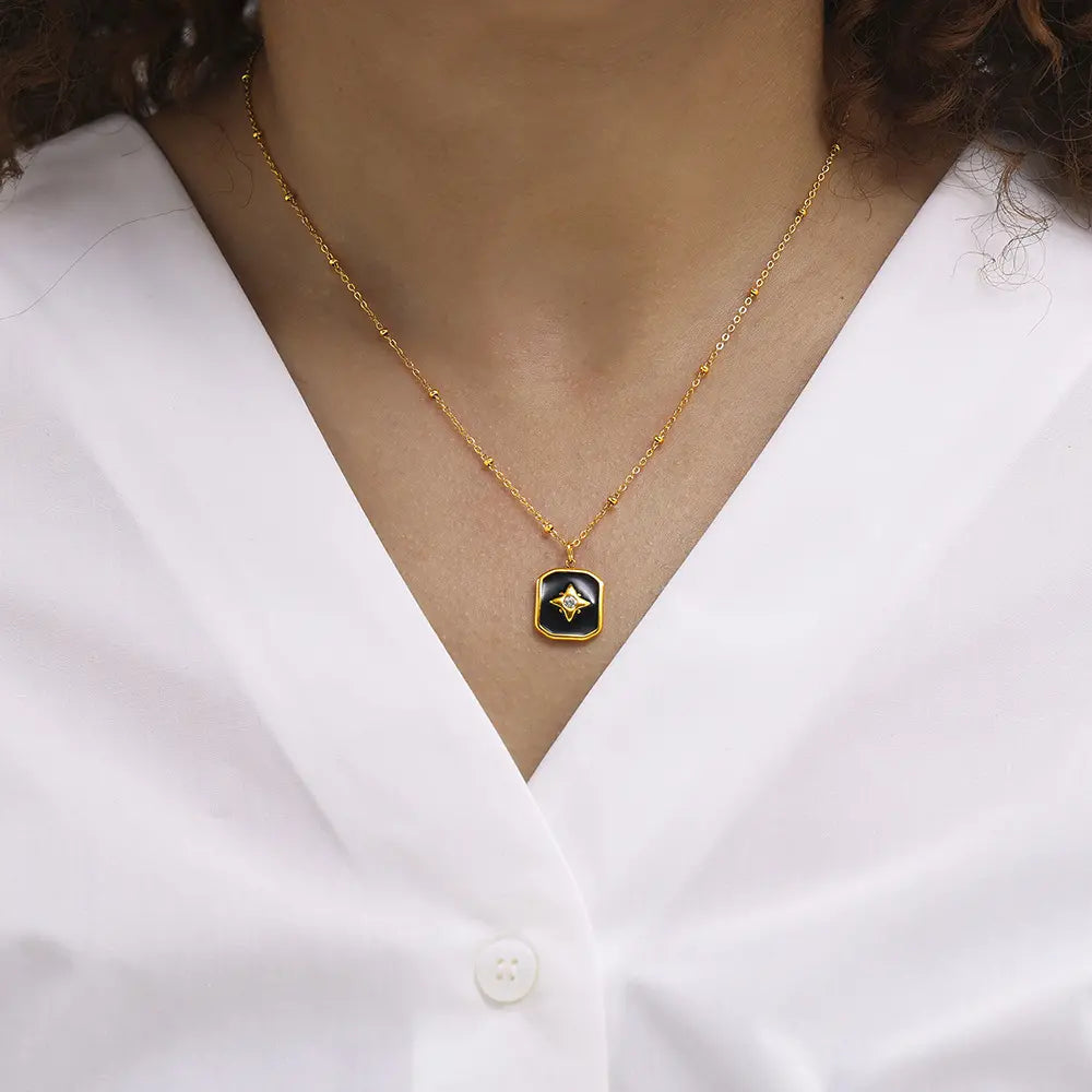 Model wearing a gold necklace with a black enamel star pendant, paired with a classic white blouse.