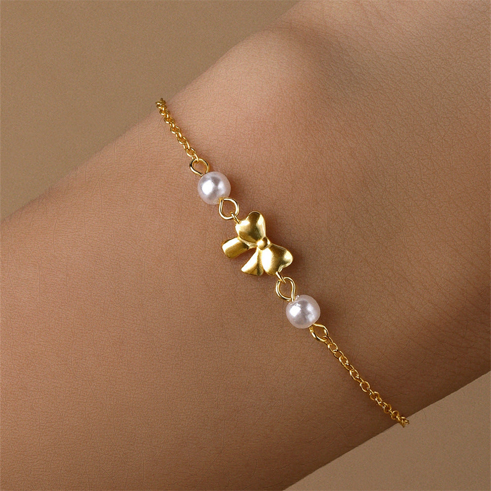 Gold bow charm bracelet with pearls, styled on a wrist to showcase its refined and minimalist elegance.