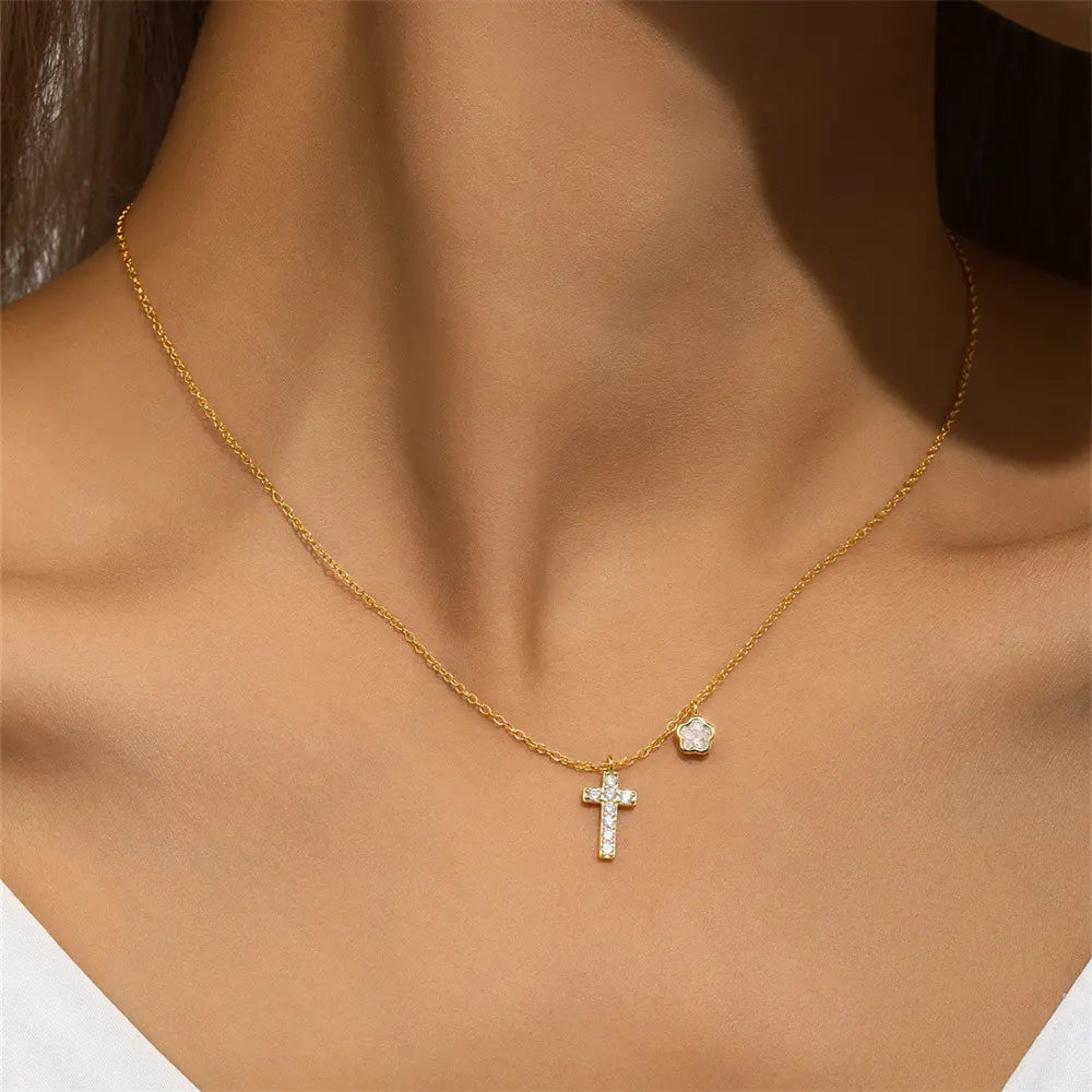 Close-up of a woman wearing a gold cross necklace with a small floral charm, crafted in 925 sterling silver with cubic zirconia accents.