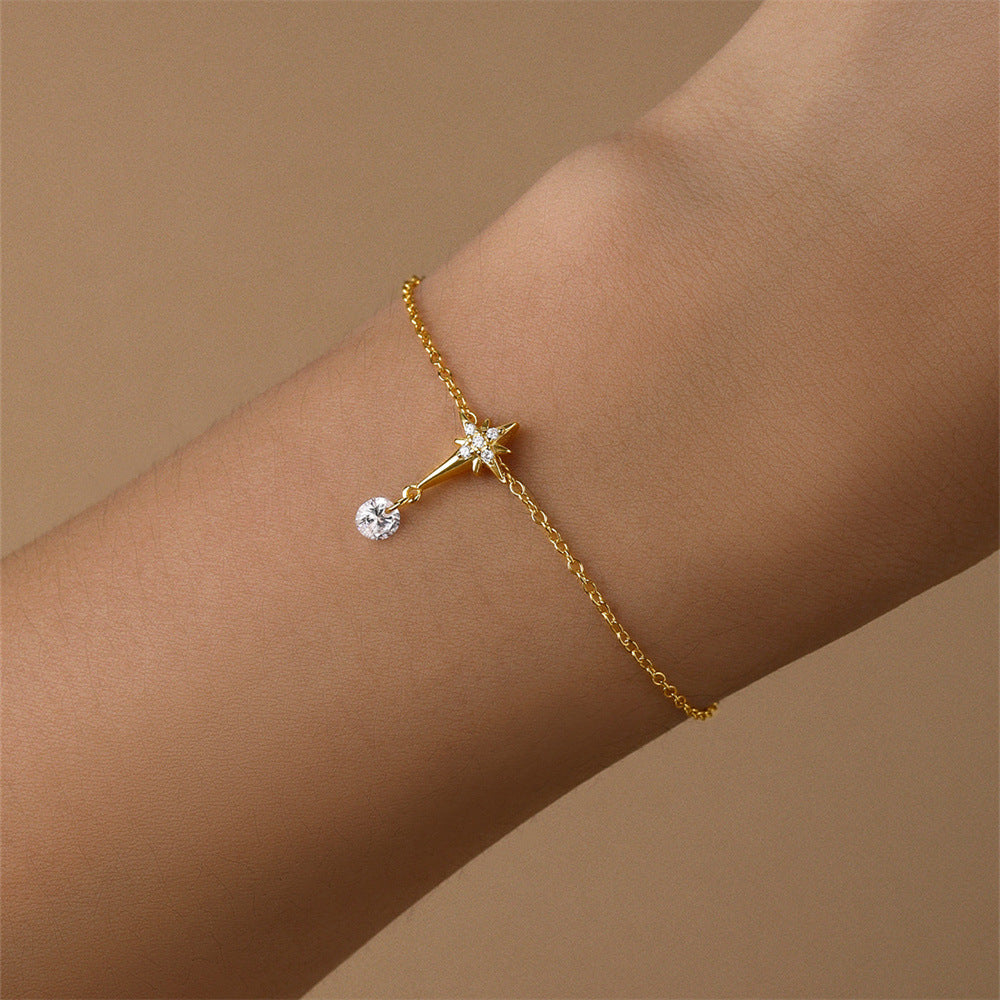 Delicate gold star charm bracelet with zirconia drop, worn on wrist for an elegant look.