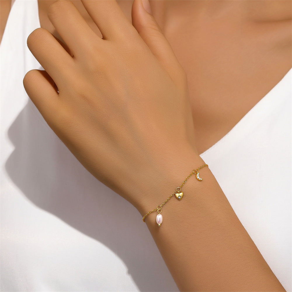 Close-up of a model wearing a gold-plated charm bracelet with a pearl, heart, and crescent moon design.