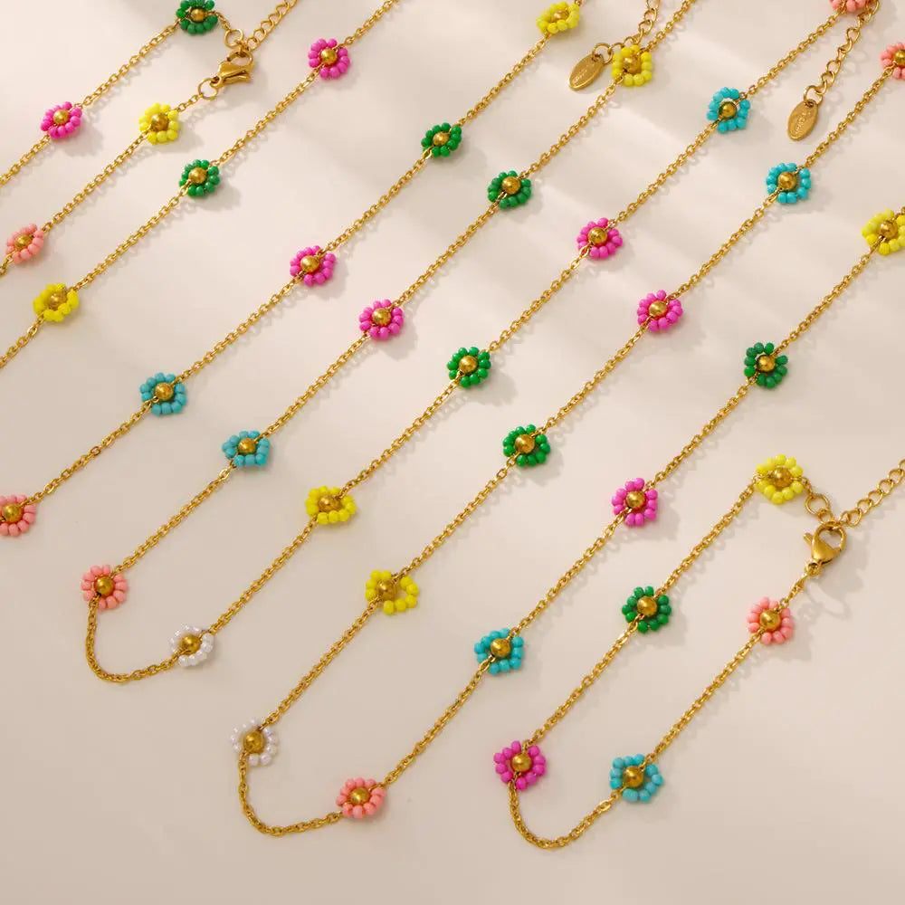 Multiple gold necklaces with colorful flower bead details arranged neatly on a beige surface.