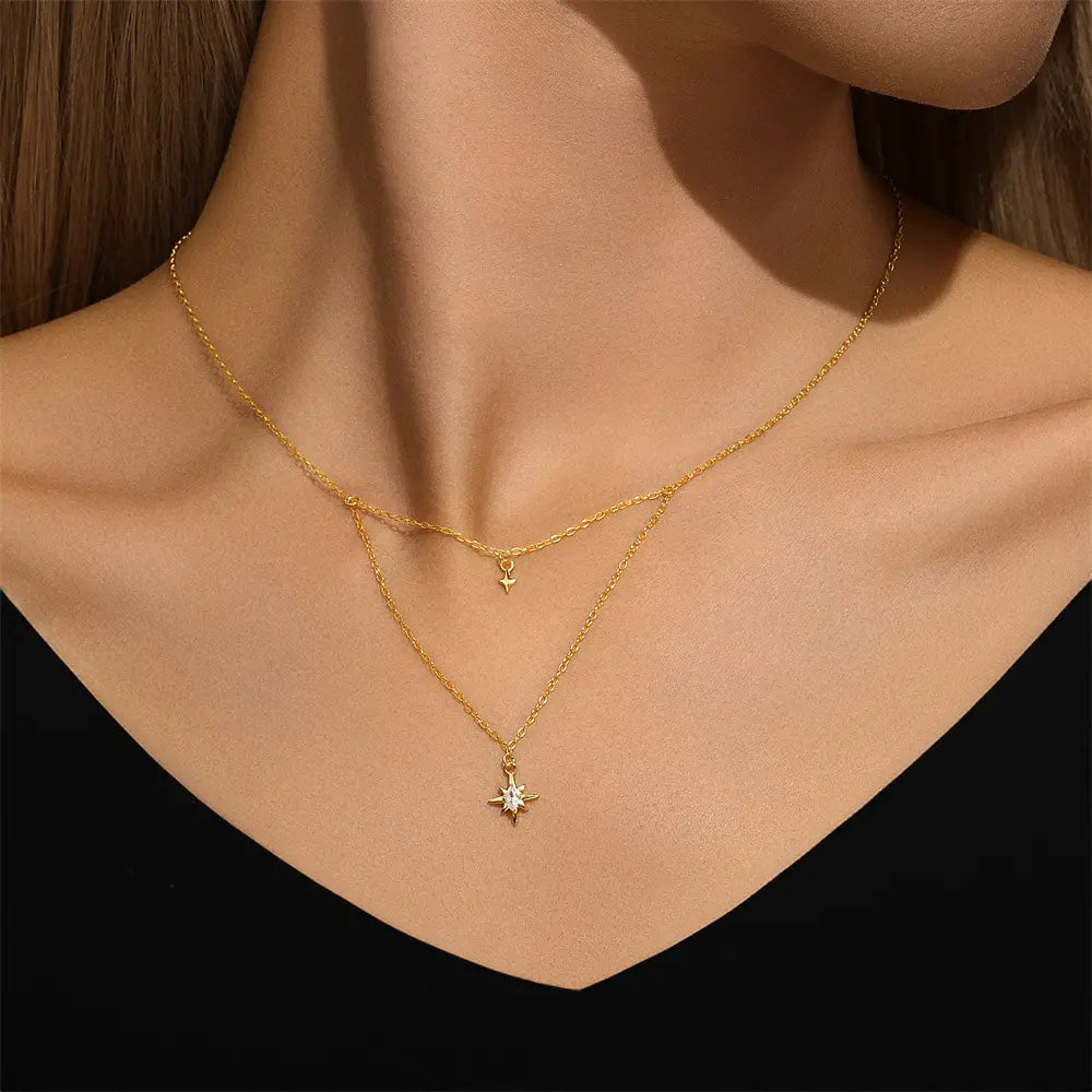 Model wearing a gold layered necklace featuring a starburst charm and a small star pendant, elegant jewelry for a celestial-inspired look.