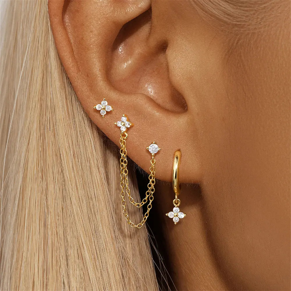 Close-up of a woman's ear showcasing the set of gold earrings, featuring a delicate flower stud, a cascading chain earring, and a hoop with a dangling flower charm.