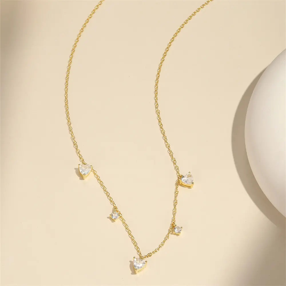 Elegant gold-plated heart pendant necklace displayed on a soft beige background, featuring 925 sterling silver and sparkling stones.