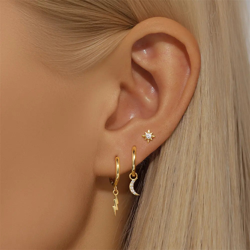 Close-up of a model's ear wearing the three-piece gold earring set: a star stud at the top, followed by the crescent moon charm hoop and lightning bolt charm hoop.