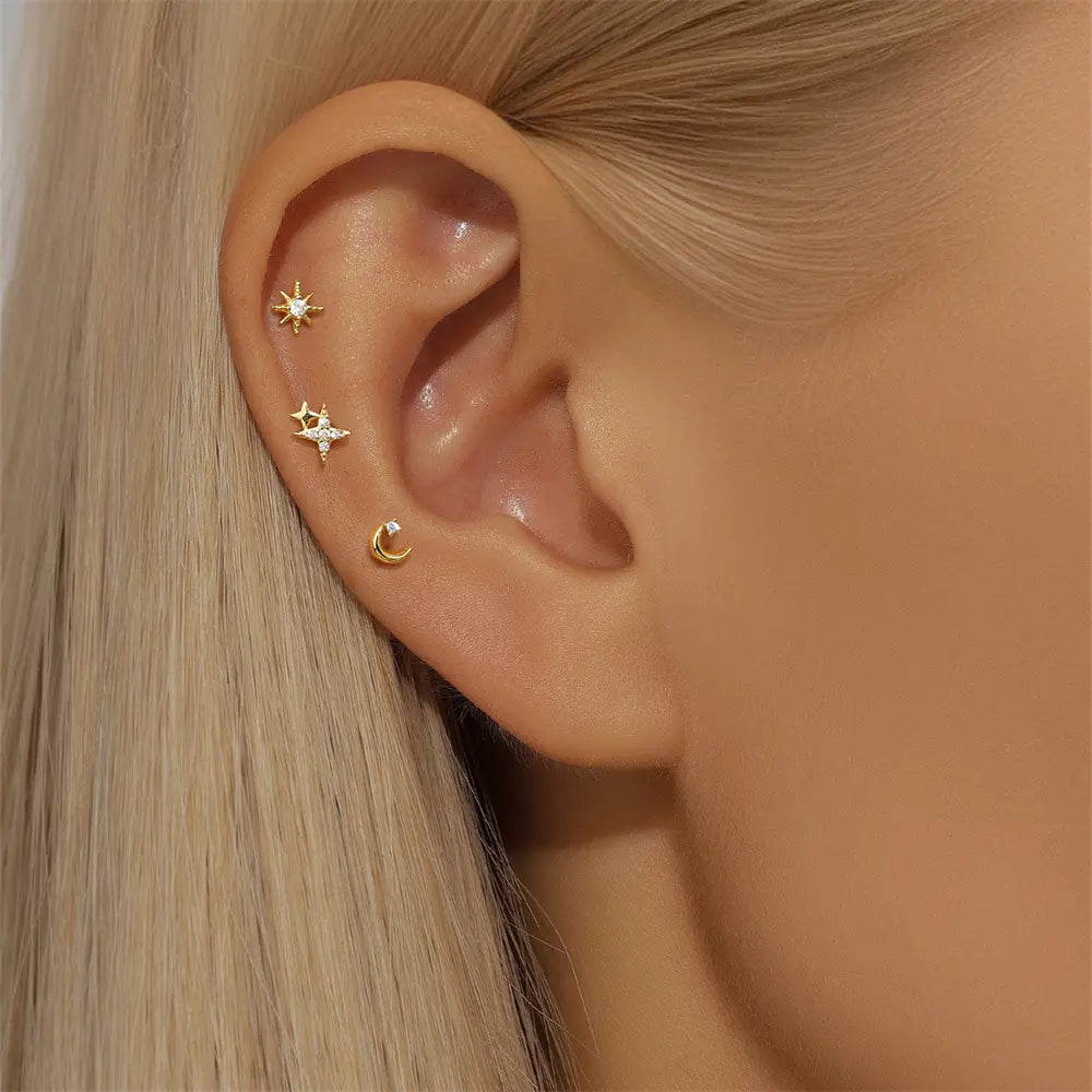 Close-up of a woman's ear adorned with gold star and crescent moon stud earrings, showcasing their elegant and delicate design.