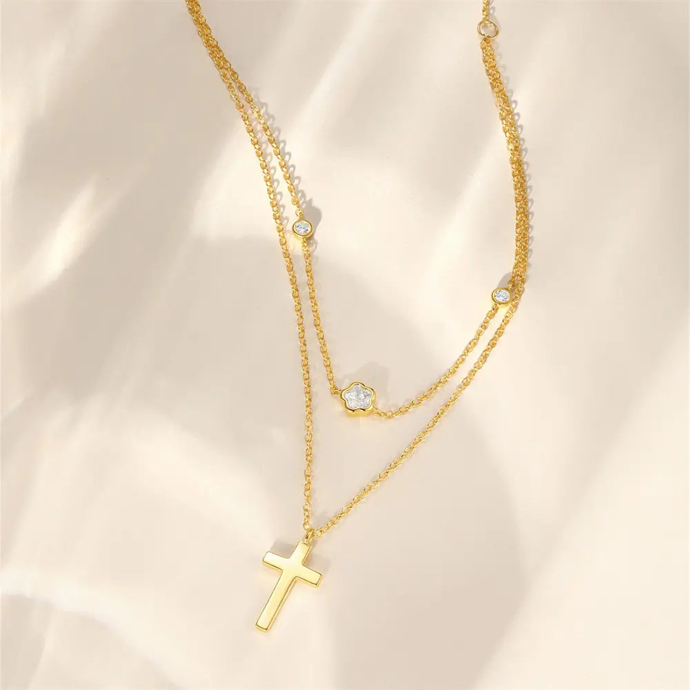 Close-up of a double-layer gold necklace featuring a cross and floral charms on a soft beige background, crafted from 925 sterling silver.