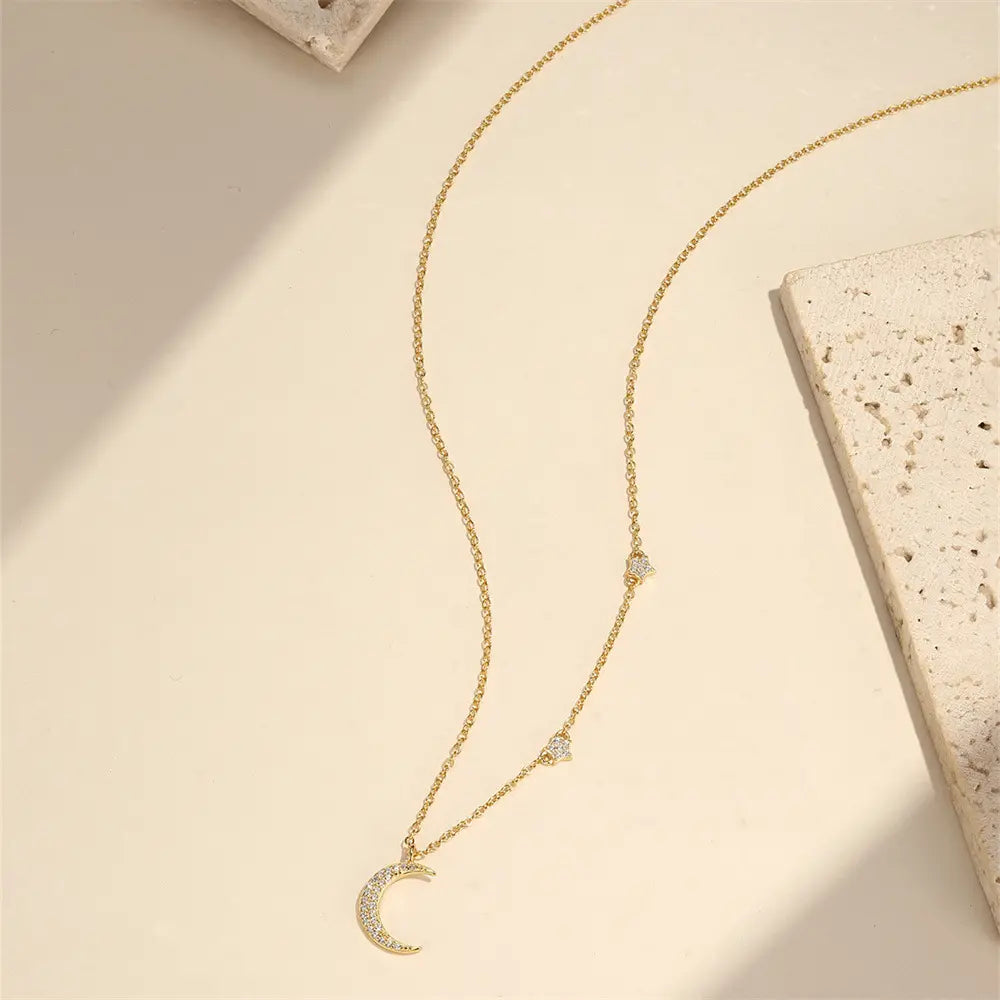 Flat lay of a crescent moon necklace with gold finish, featuring minimalist star designs and cubic zirconia stones.