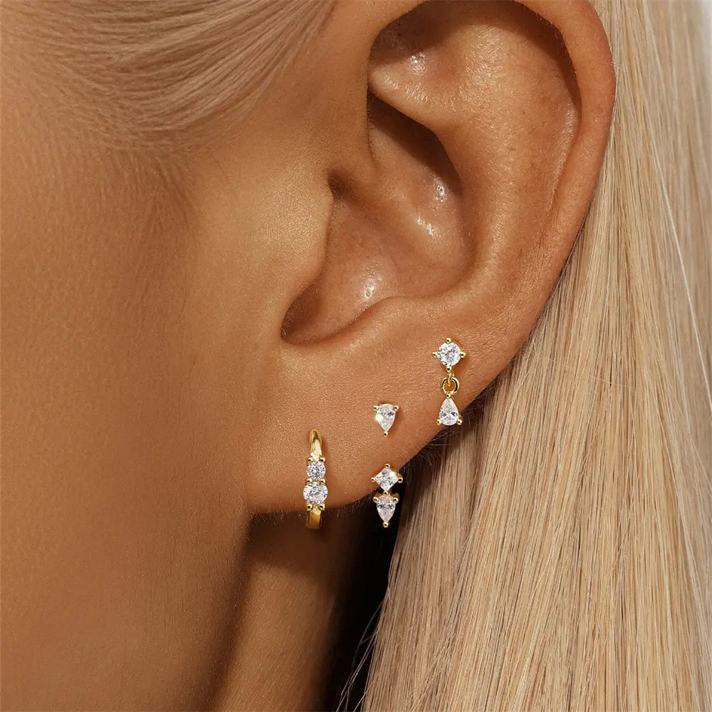 Woman’s ear wearing a gold three-piece earring set, featuring a hoop, drop earring, and stud.