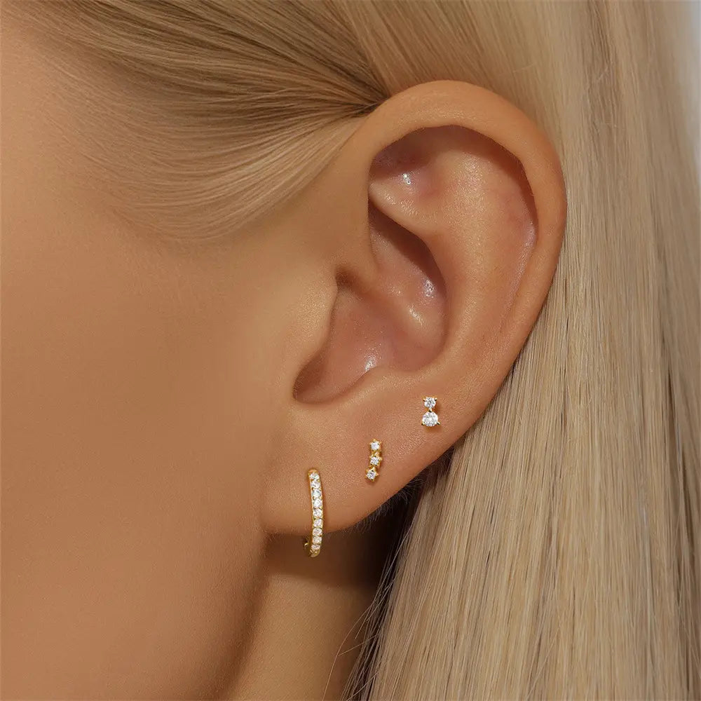 Model showcasing three gold earrings: a sparkling stud, a star-shaped row earring, and a delicate pave hoop, styled in an ear stack.