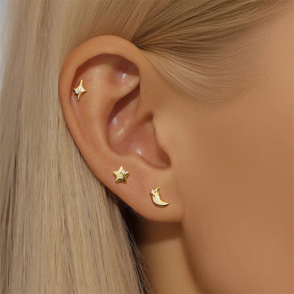  A close-up of a model’s ear styled with the star, starburst, and crescent moon gold-plated stud earrings, showcasing a celestial-themed ear stack.