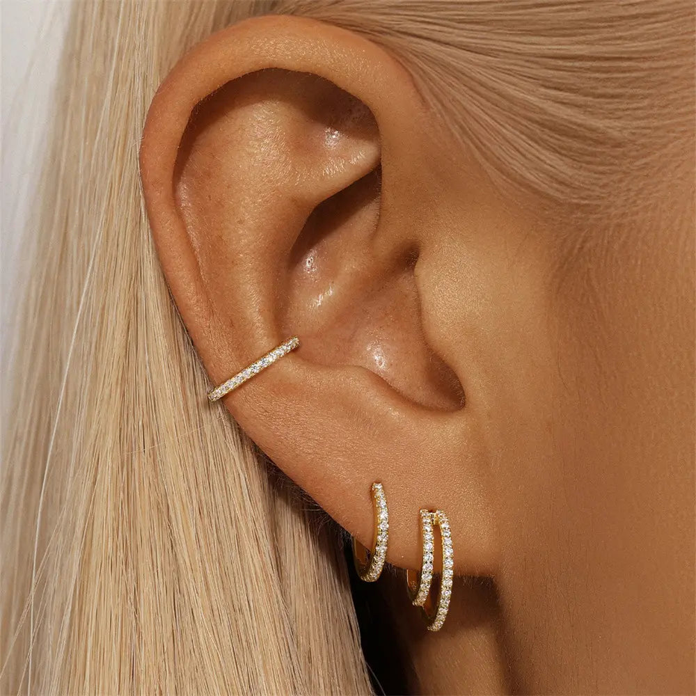 Woman's ear adorned with a gold hoop, open cuff, and double-layered stud earring set