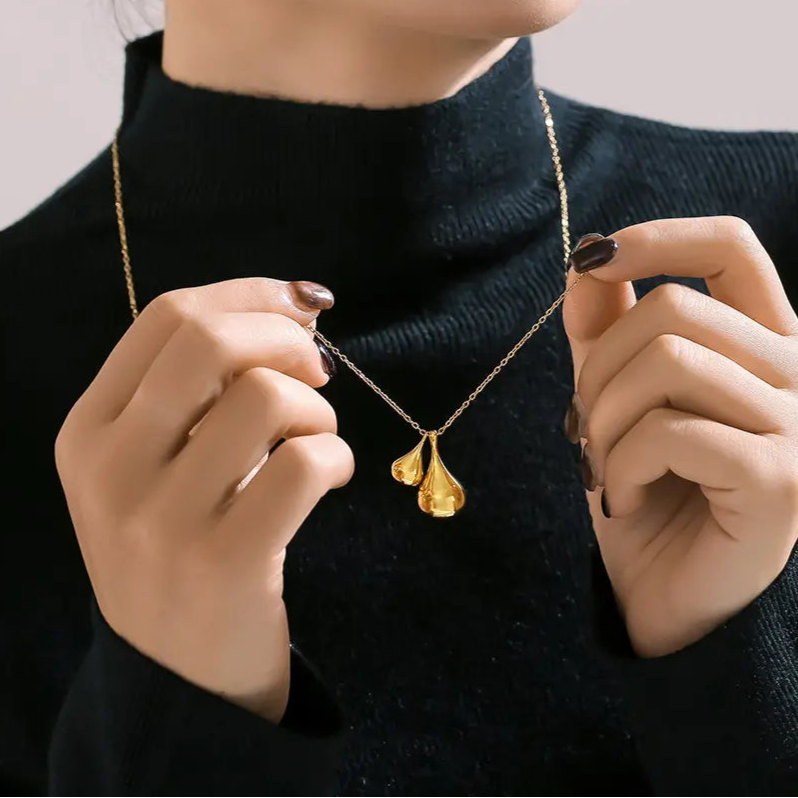 Collection of golden titanium plated water droplet pendant necklaces with varying sizes of droplets on a beige background