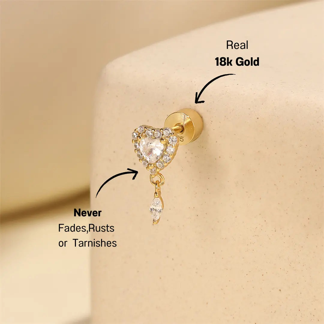 Heart-shaped zircon cartilage earring with a dangling zircon charm displayed on a soft beige background, crafted in gold-plated 925 sterling silver.