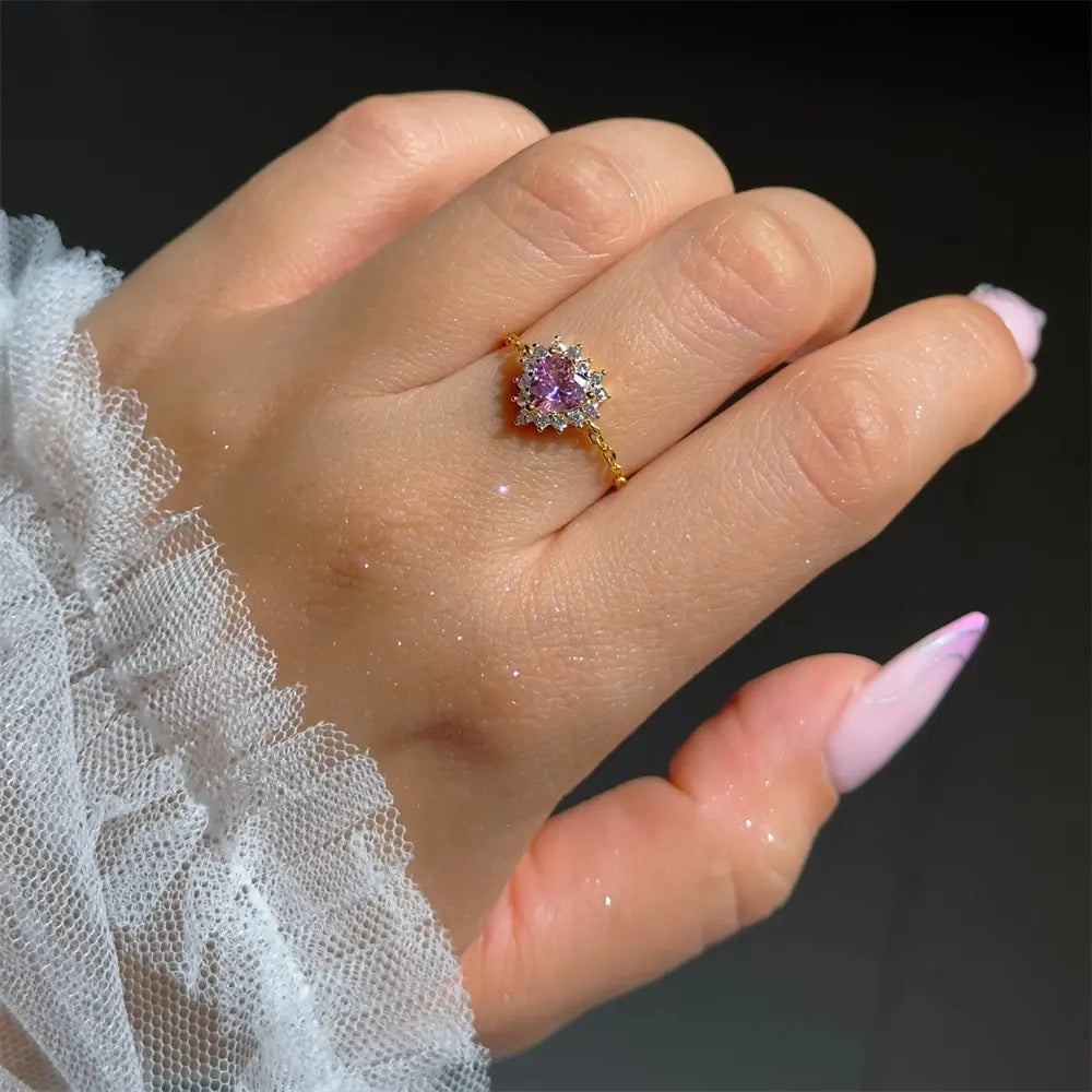 Close-up image of a model's hand wearing a gold-plated 925 sterling silver ring with a heart-shaped pink zirconia stone and clear zirconia accents.