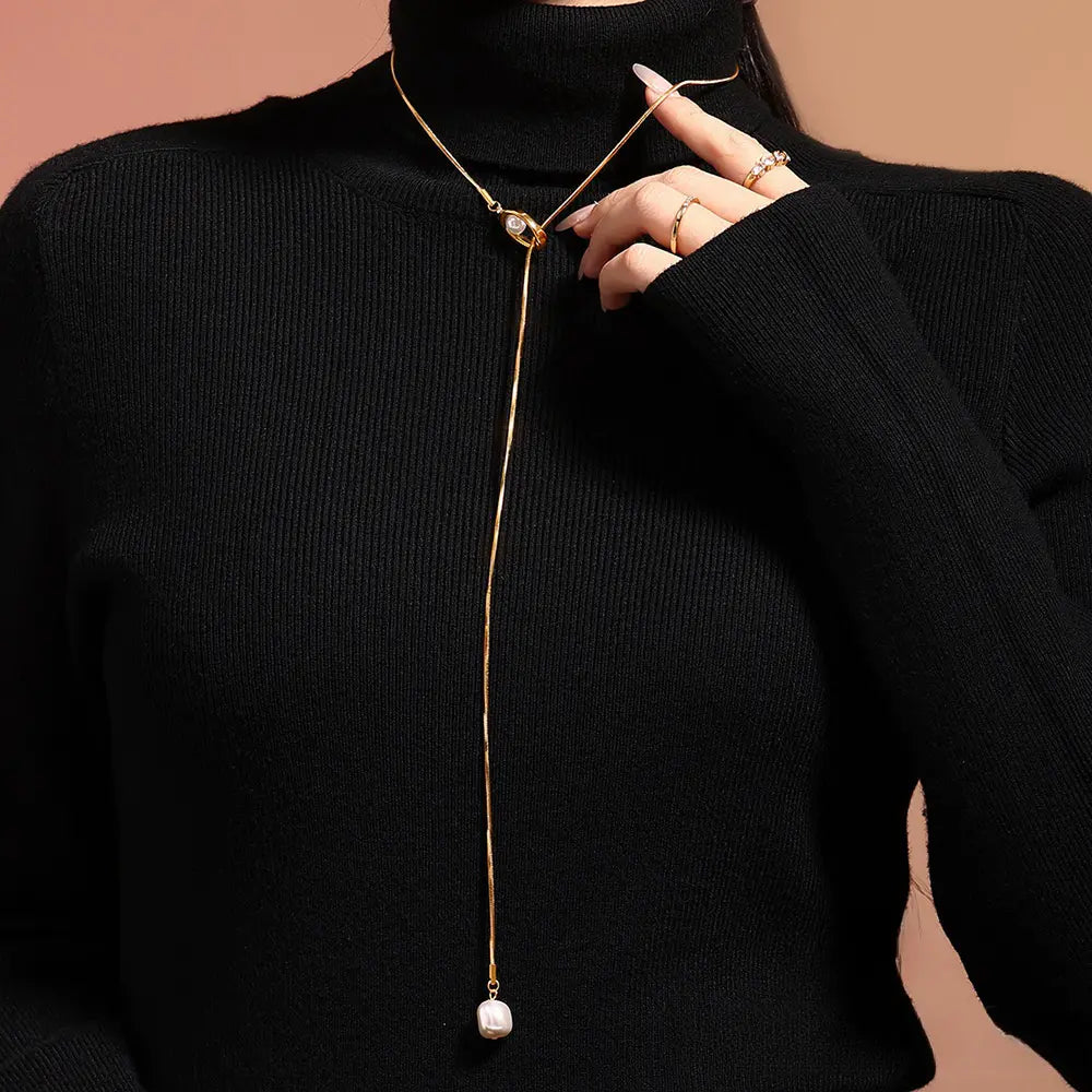 A model wearing a 14k gold-plated titanium necklace with a white pearl drop pendant on a black sweater