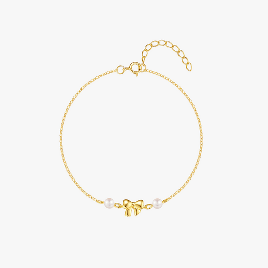 Delicate gold bracelet with a bow charm and pearl accents, featuring a timeless and elegant design for everyday wear or special occasions.