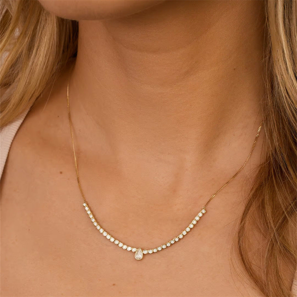  A woman wearing a gold teardrop necklace with sparkling zircon stones. Perfect for layering or solo wear for a chic and minimalist look.