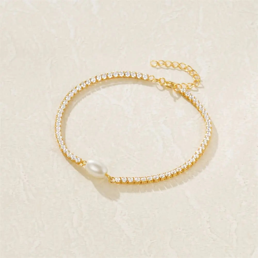 Elegant pearl drop bracelet with delicate gold chain on a soft textured surface.