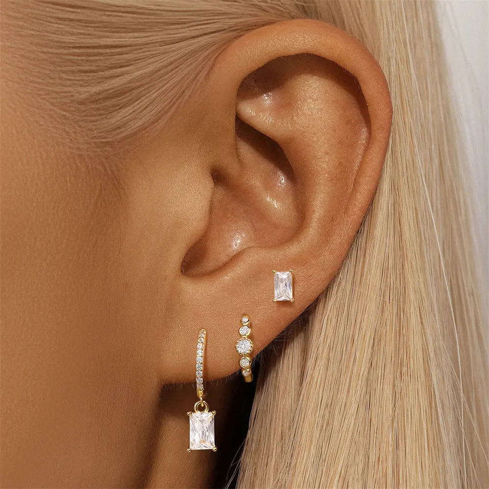 Close-up of a model wearing a gold-plated sterling silver three-piece earring set with sparkling crystals.